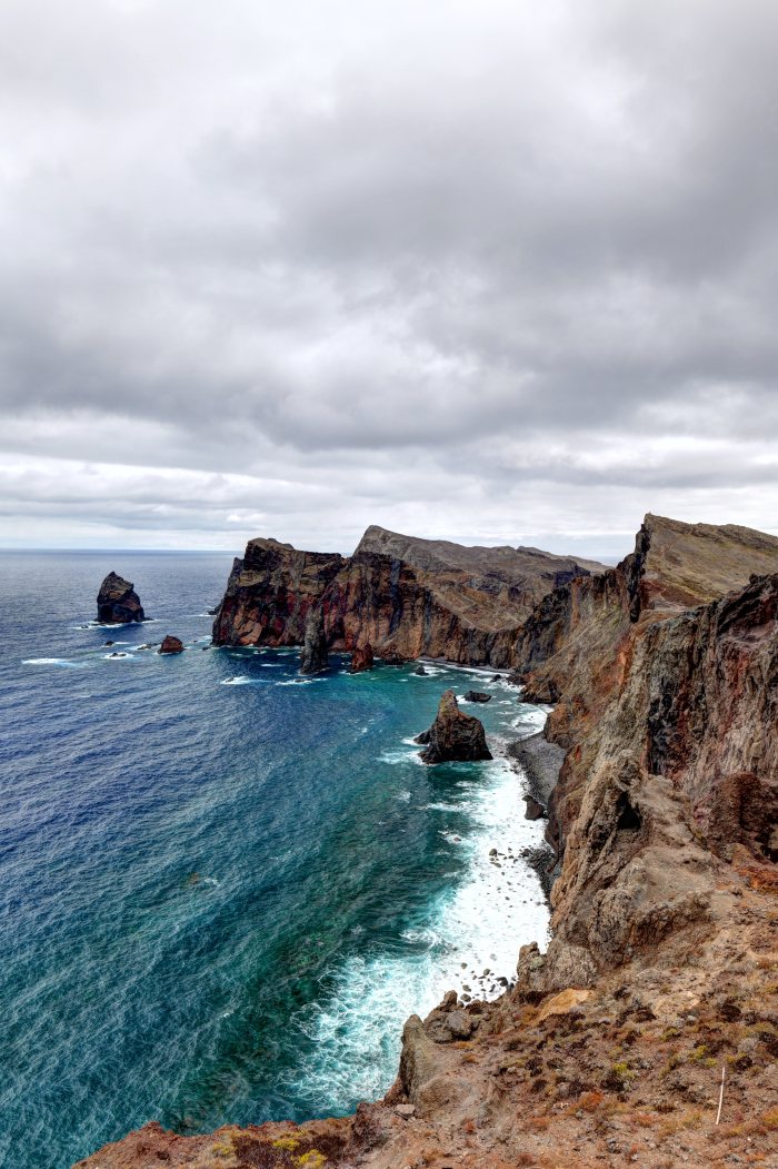 Onde dell'oceano che si infrangono su rocce costiere sotto un cielo nuvoloso