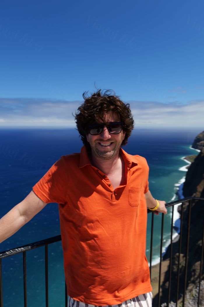 Uomo sorridente in un punto panoramico con vista sul mare e scogliere